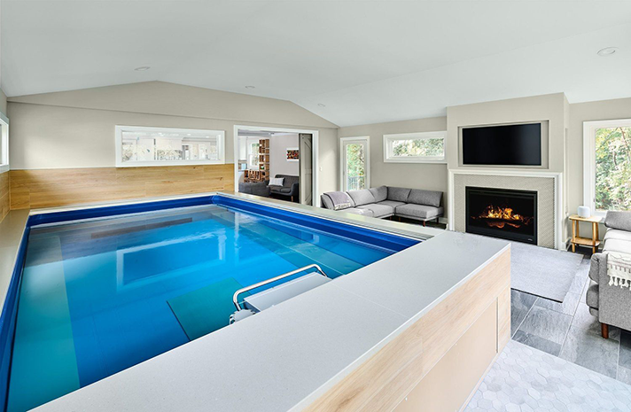 A large indoor swimming pool in a living room next to a fireplace.