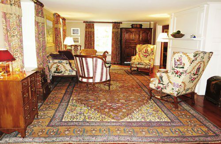 A living room with a rug , chairs , a dresser and a fireplace.