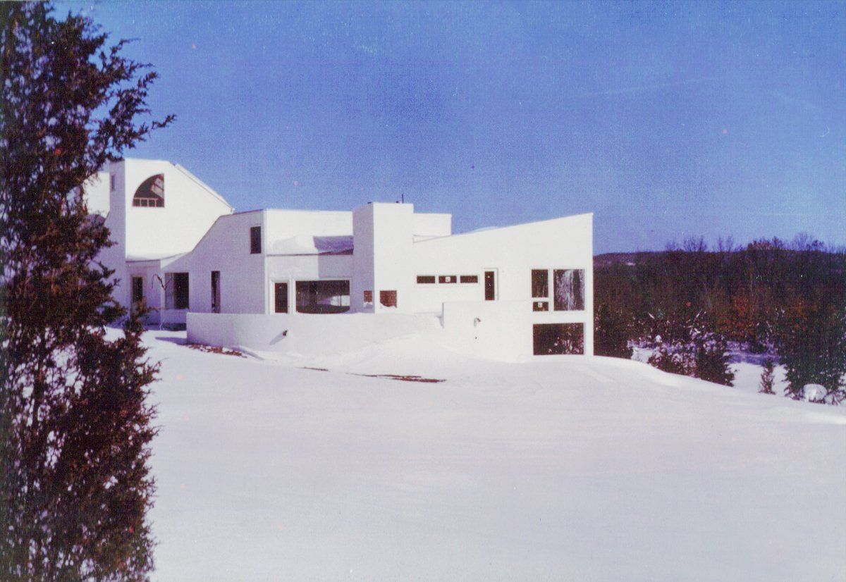 A large white house is surrounded by snow and trees
