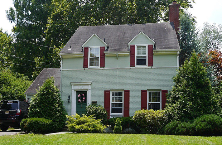A green house with red shutters and a jeep parked in front of it
