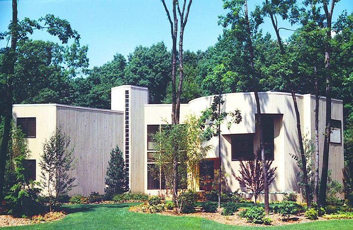 A large white house is surrounded by trees on a sunny day