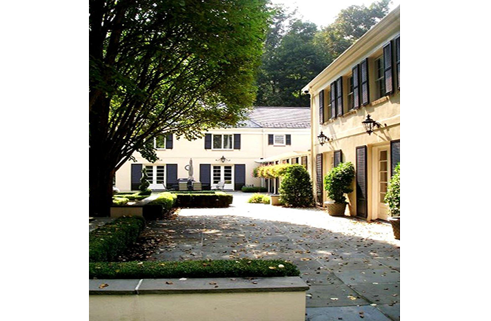 A white house with black shutters is surrounded by trees