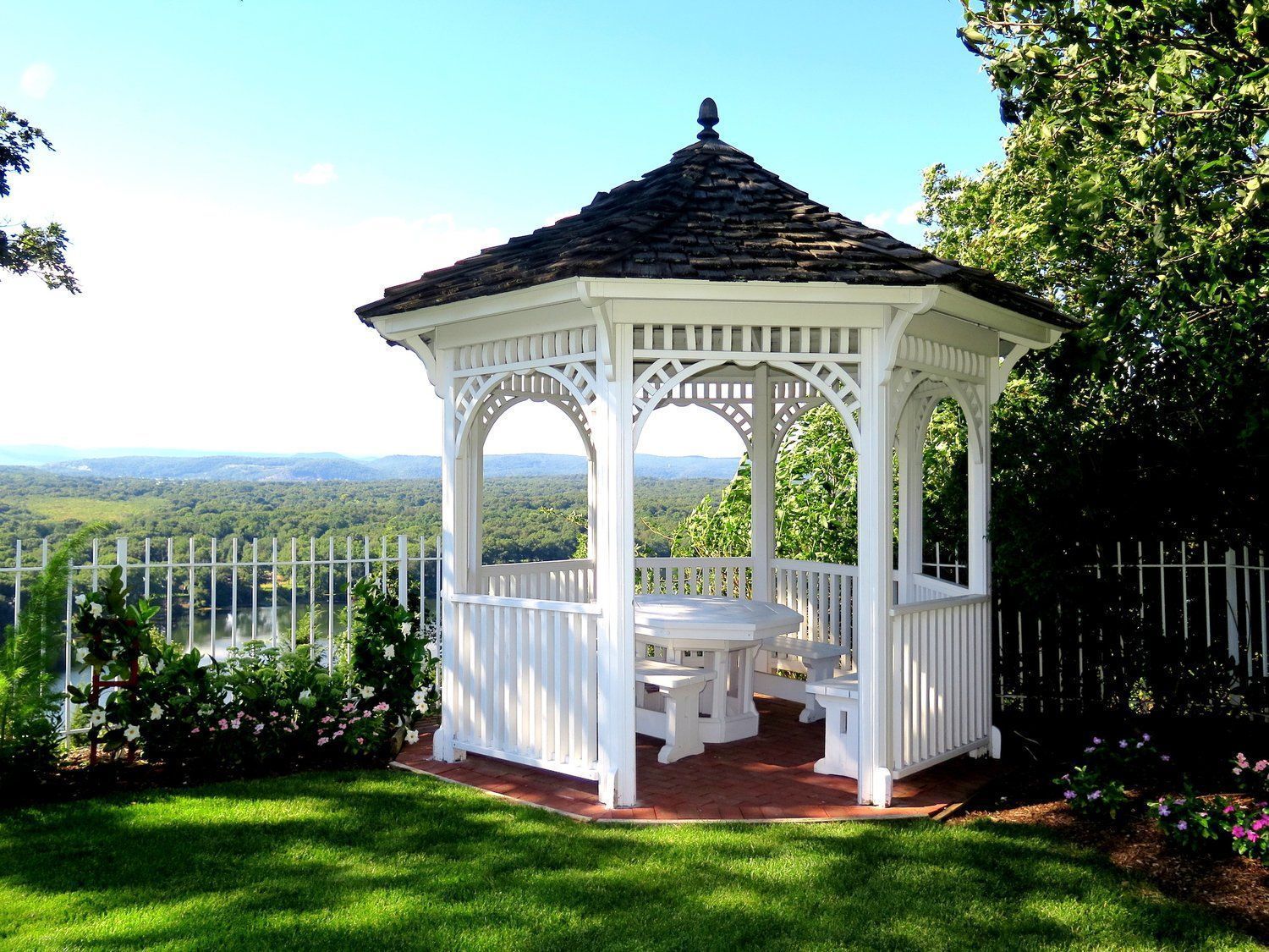A white gazebo with a table and benches in a lush green yard