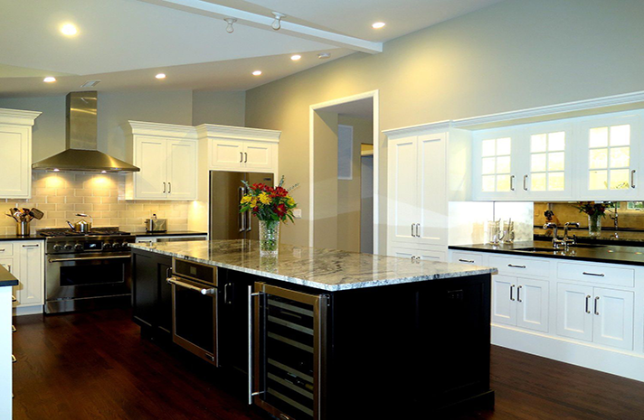 A kitchen with white cabinets , stainless steel appliances , a large island and a vase of flowers on the counter.