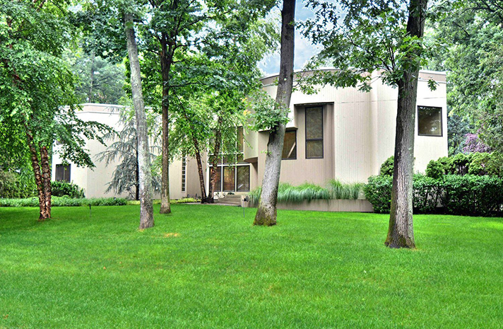 A house with a lush green lawn and trees in front of it