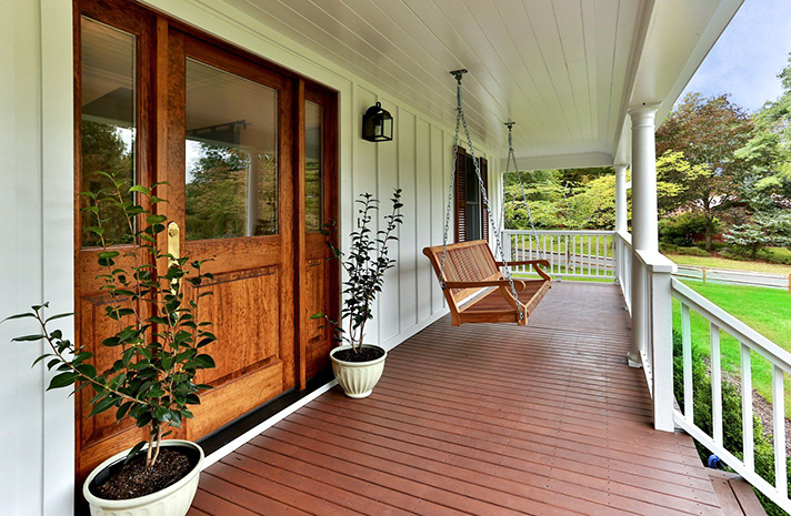 A porch with a swing hanging from the ceiling and potted plants.