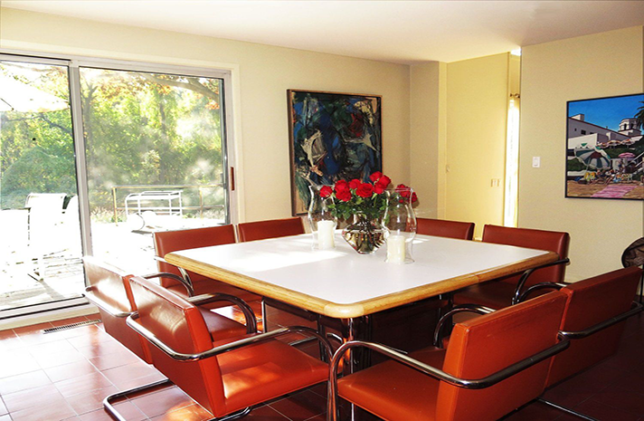 A dining room with a table and chairs and a painting on the wall
