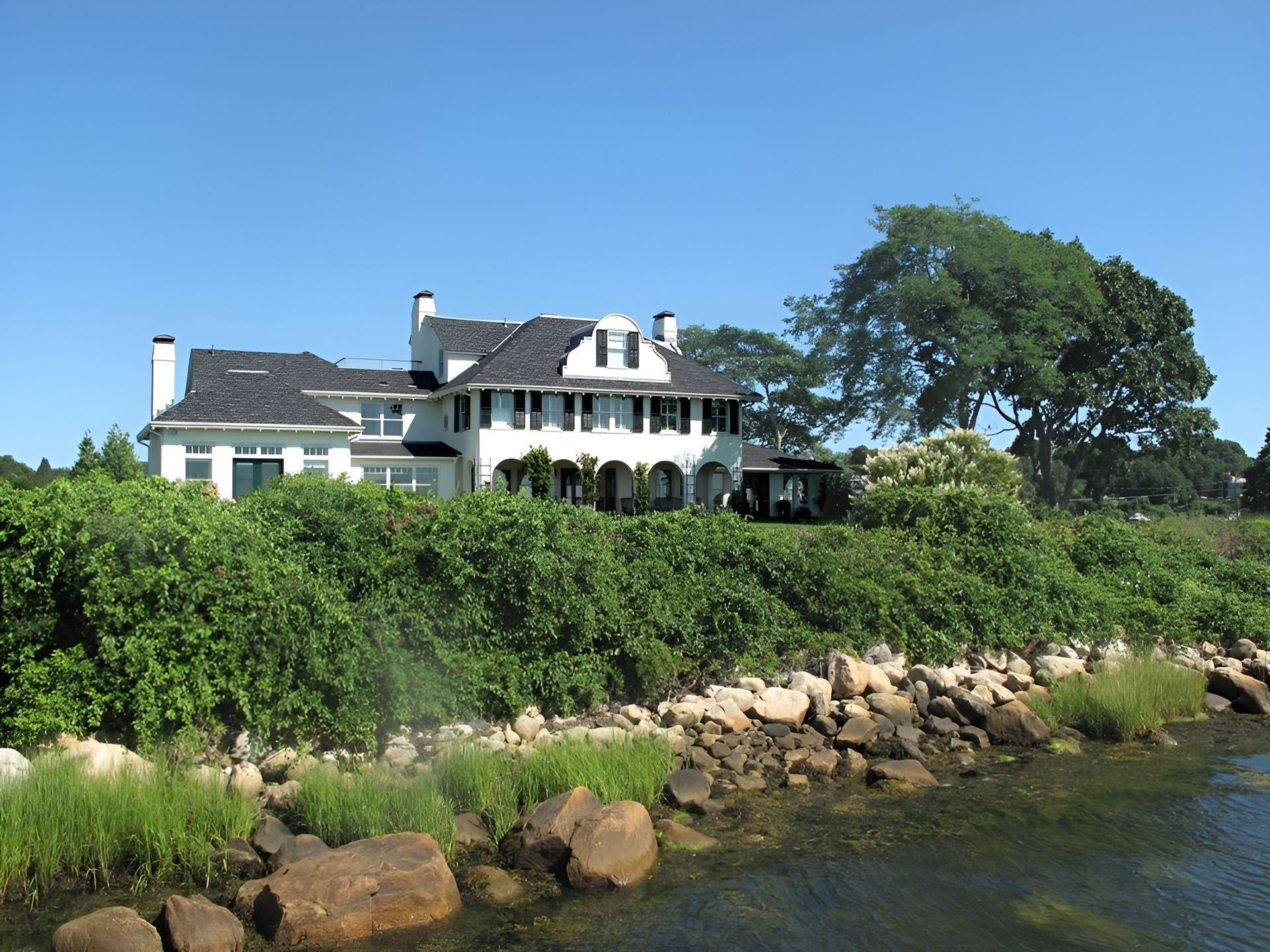 A large white house sits next to a body of water