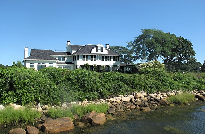 A large white house sits on the shore of a body of water