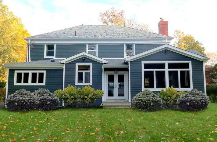 A large blue house with a screened in porch is sitting on top of a lush green lawn.