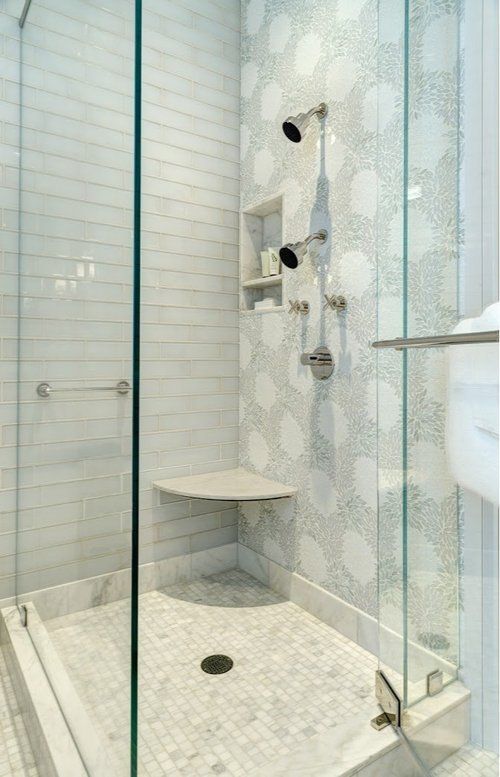 A bathroom with a walk in shower with a glass door and a seat.