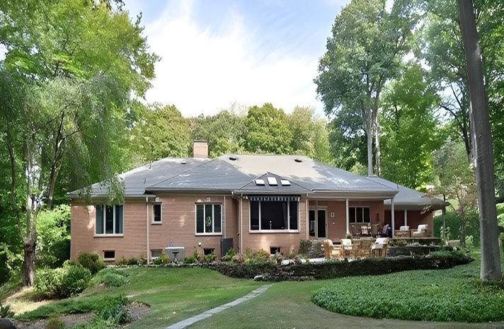 A large brick house sits in the middle of a lush green forest