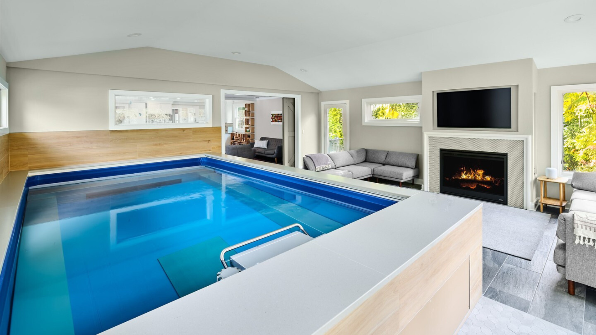 A large indoor swimming pool in a living room next to a fireplace.
