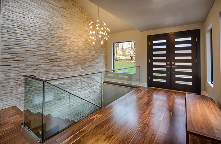 A hallway with hardwood floors , stairs , and a glass railing.