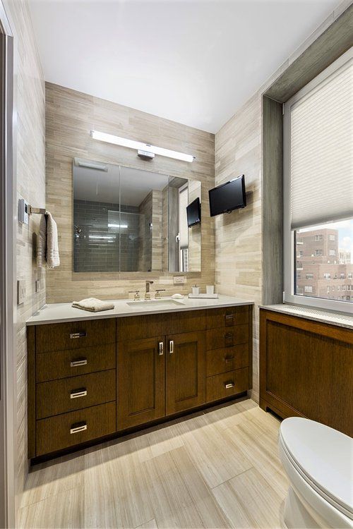 A bathroom with a toilet , sink , mirror and television.
