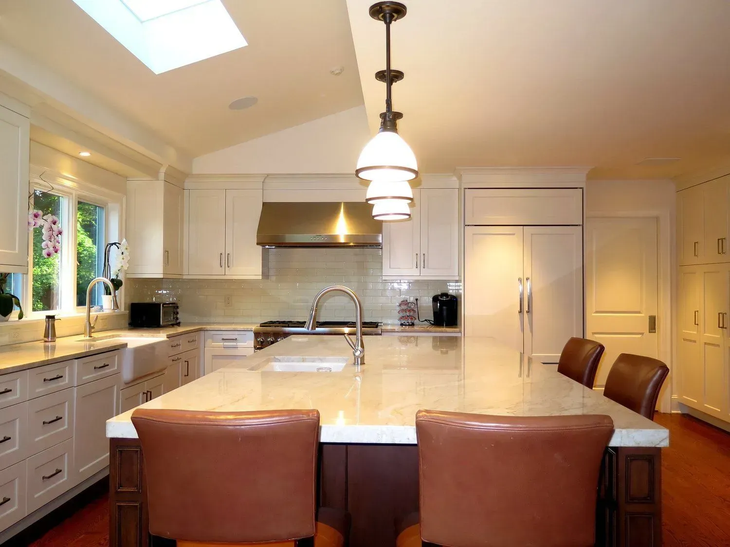 A kitchen with white cabinets and brown chairs and a large island