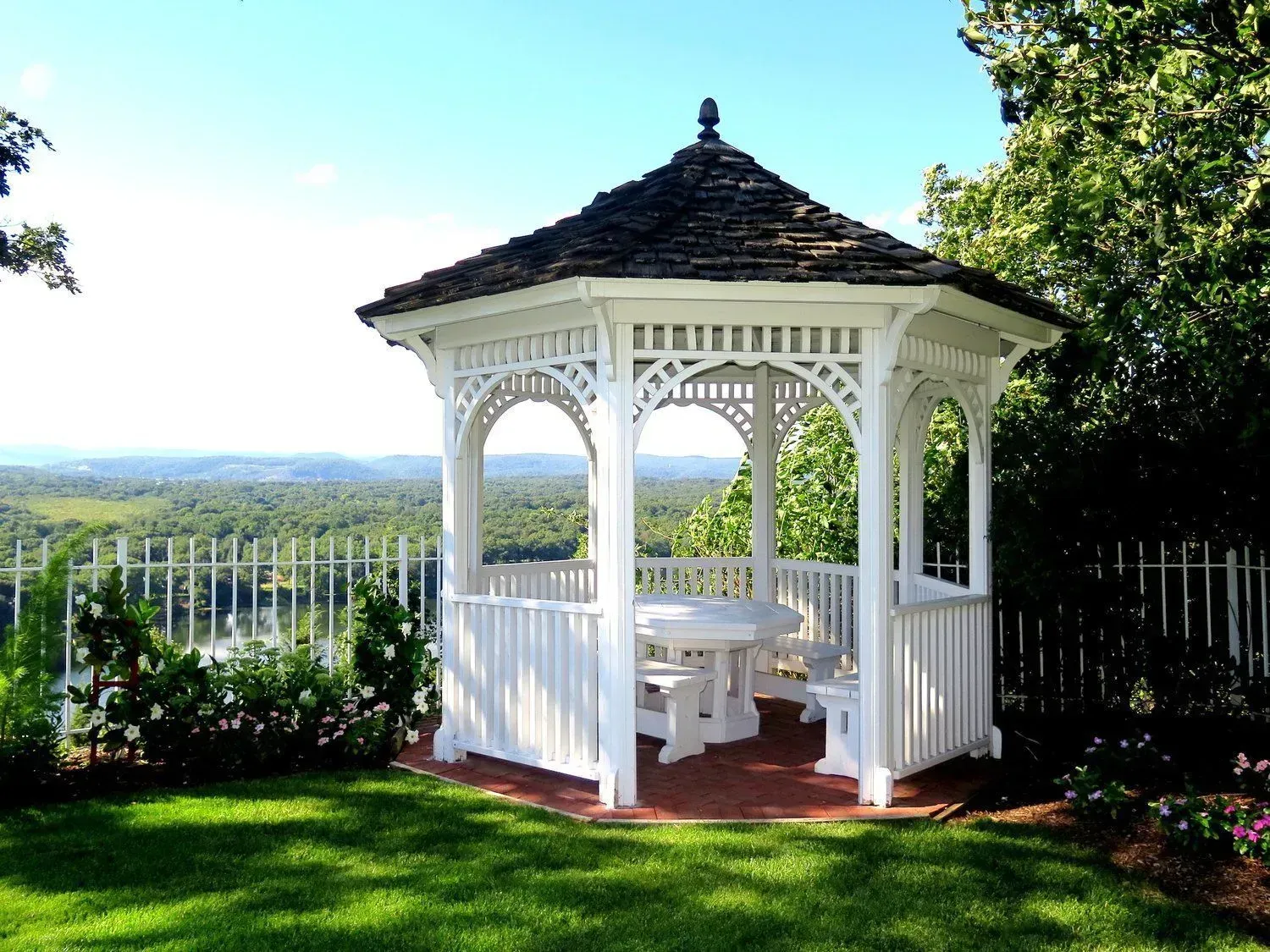 A white gazebo sits in the middle of a lush green field