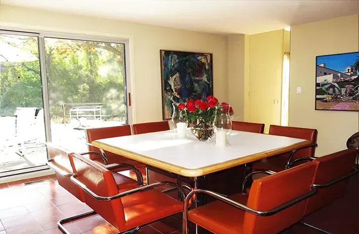 A dining room with a table and chairs and a painting on the wall.