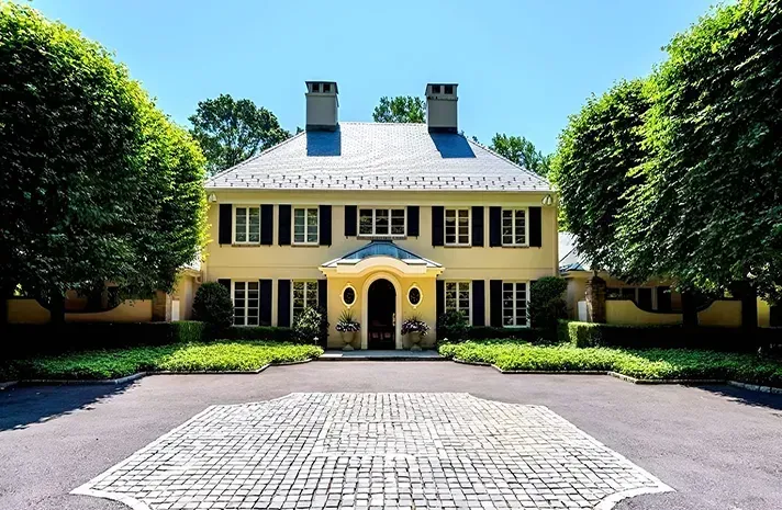 A large yellow house with black shutters is surrounded by trees