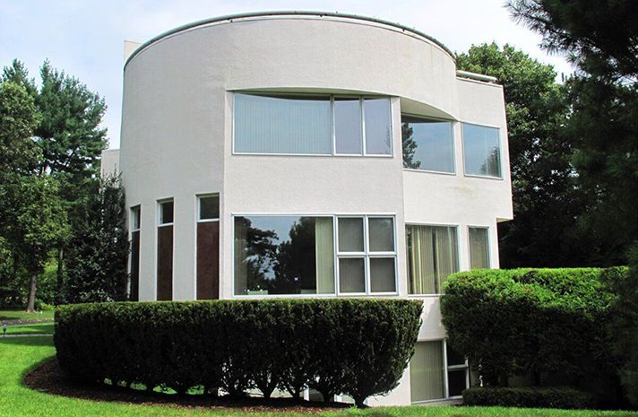 A white house with a lot of windows is surrounded by bushes