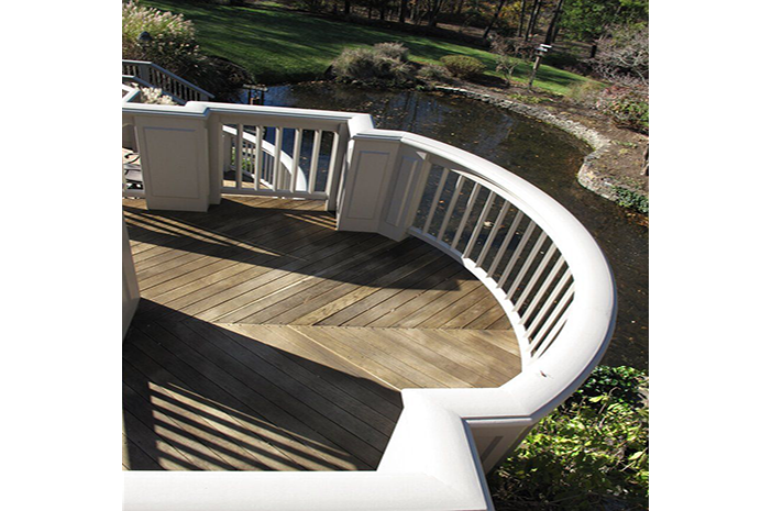 A wooden deck with a white railing overlooking a pond