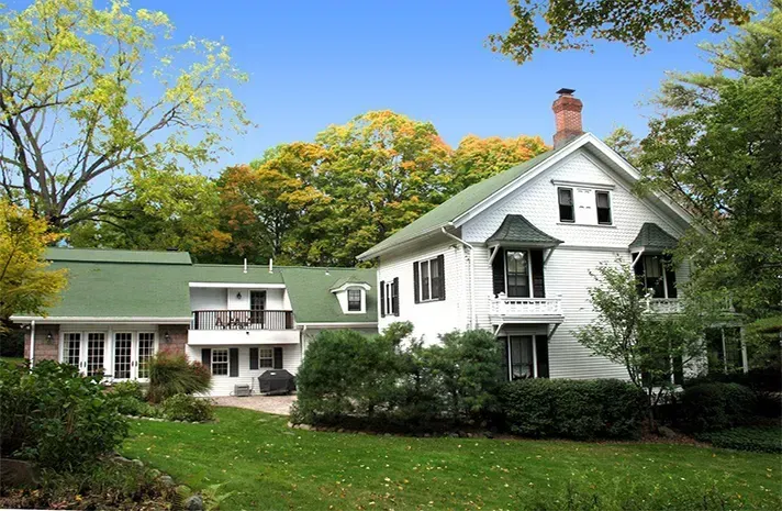 A white house with a green roof is surrounded by trees
