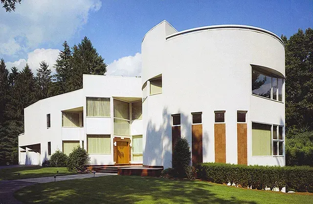 A white house with a curved roof is surrounded by trees