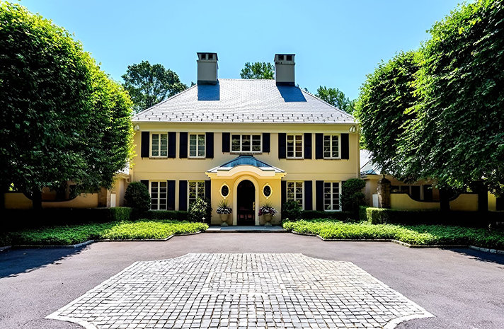 A large yellow house with black shutters is surrounded by trees