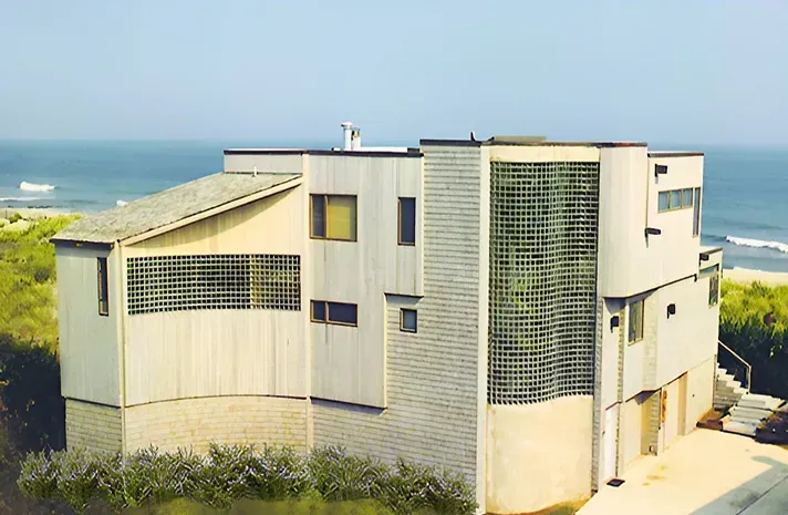 A large white house sits on a hill overlooking the ocean