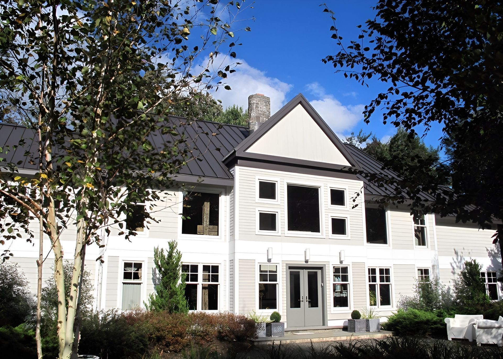 A large white house with a black roof is surrounded by trees