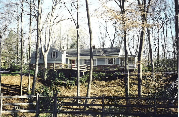 A house in the middle of a forest with a fence in front of it