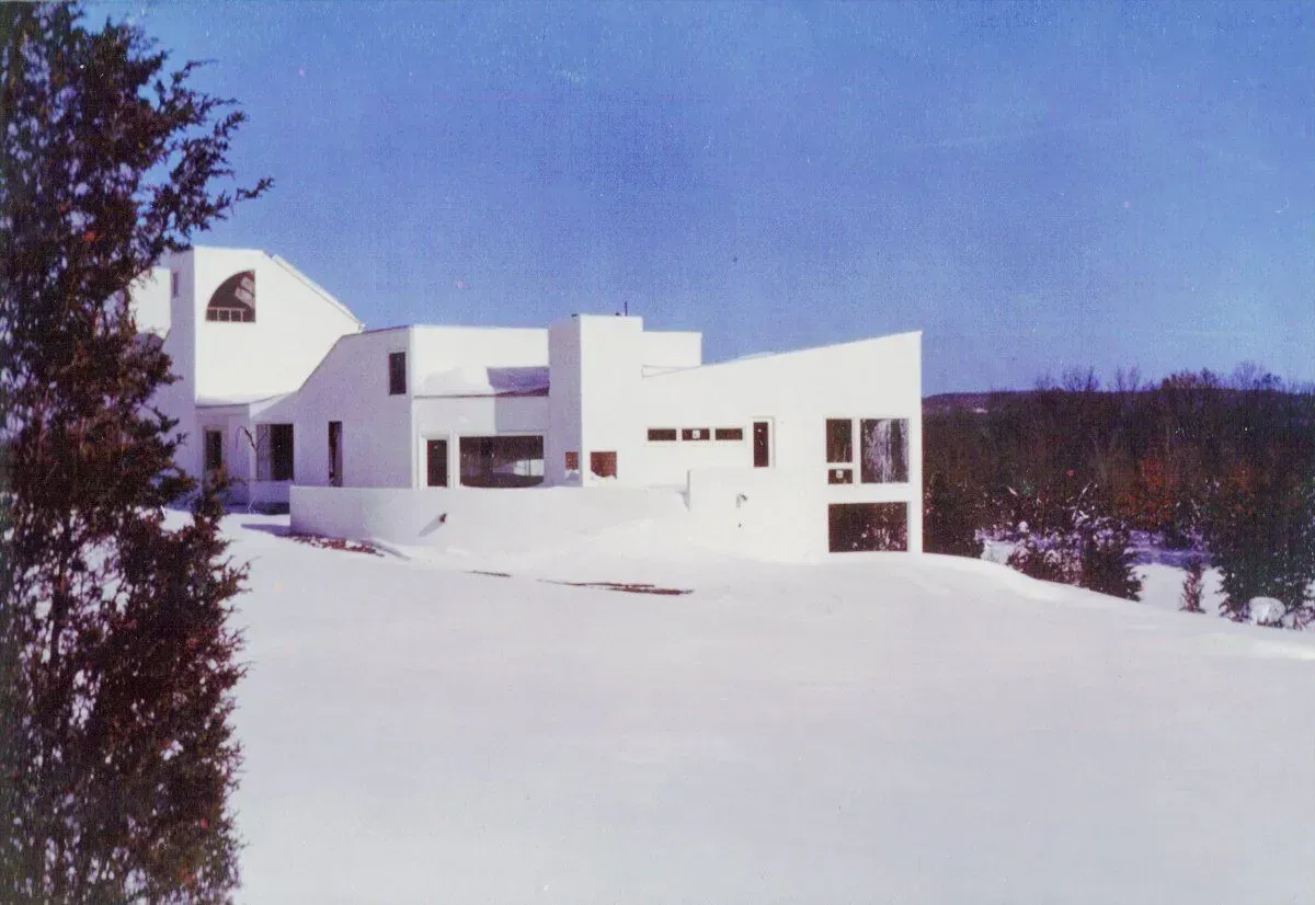 A large white house is surrounded by snow and trees