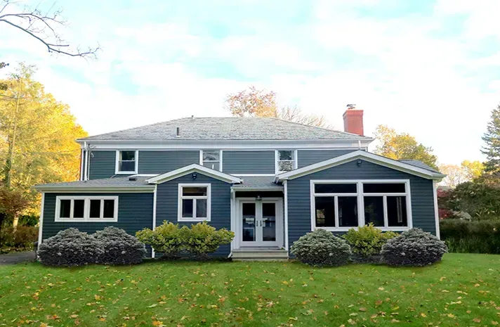 A large blue house with a lot of windows is sitting on top of a lush green lawn.