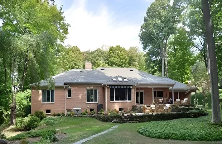 A large brick house sits in the middle of a lush green forest