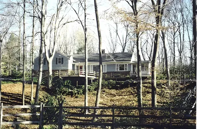 A house in the middle of a forest with a fence in front of it