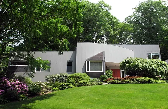 A gray house with a red door is surrounded by trees
