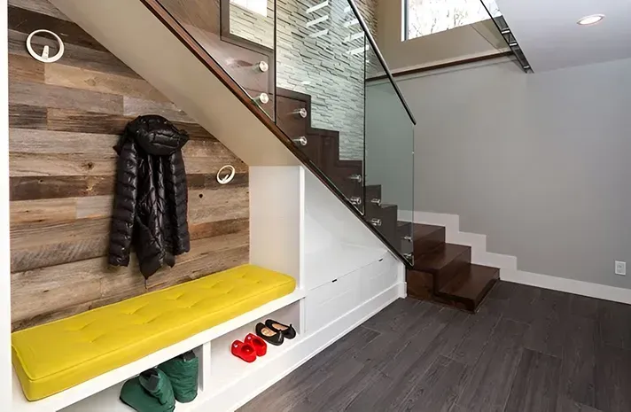 There is a bench under the stairs with a yellow cushion.