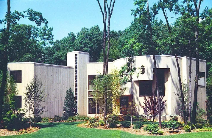 A large white house is surrounded by trees and grass