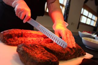 A chef is cutting a large piece of delicious meat on a cutting board.