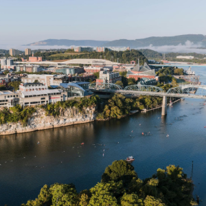 Riverfront cityscape with a bridge spanning a wide blue river, hills in the background, and buildings along the shore