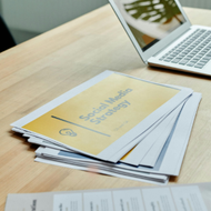 Brochures on a table beside an open laptop in a bright office setting