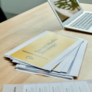 Brochures on a table beside an open laptop in a bright office setting