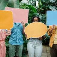 Four people hold colorful blank speech bubbles in a lush greenhouse setting