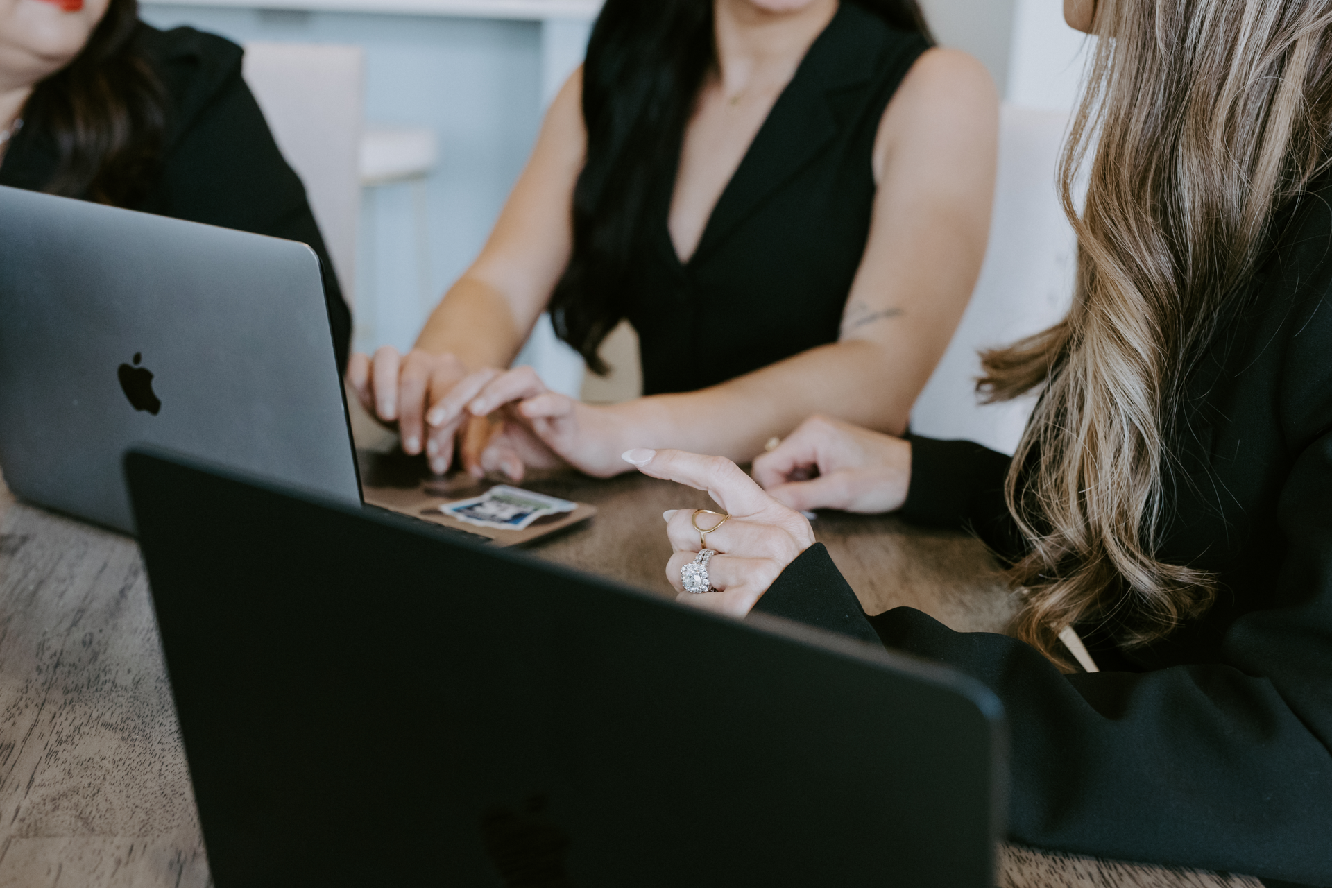 Three people in black clothing work on laptops at a conference table.