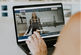 Hand using a laptop displaying a woman speaking on a website or video page