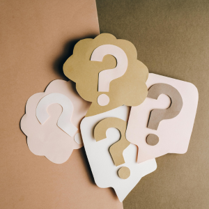 Scattered paper question marks in beige, white, and tan on a brown background
