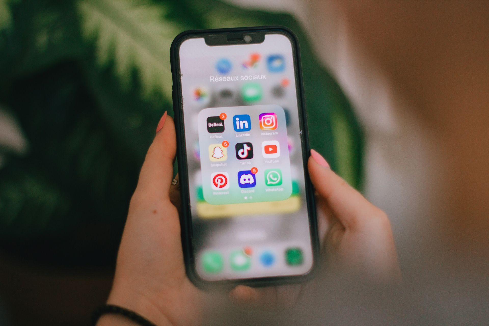 Hands holding a smartphone showing a grid of social media app icons.