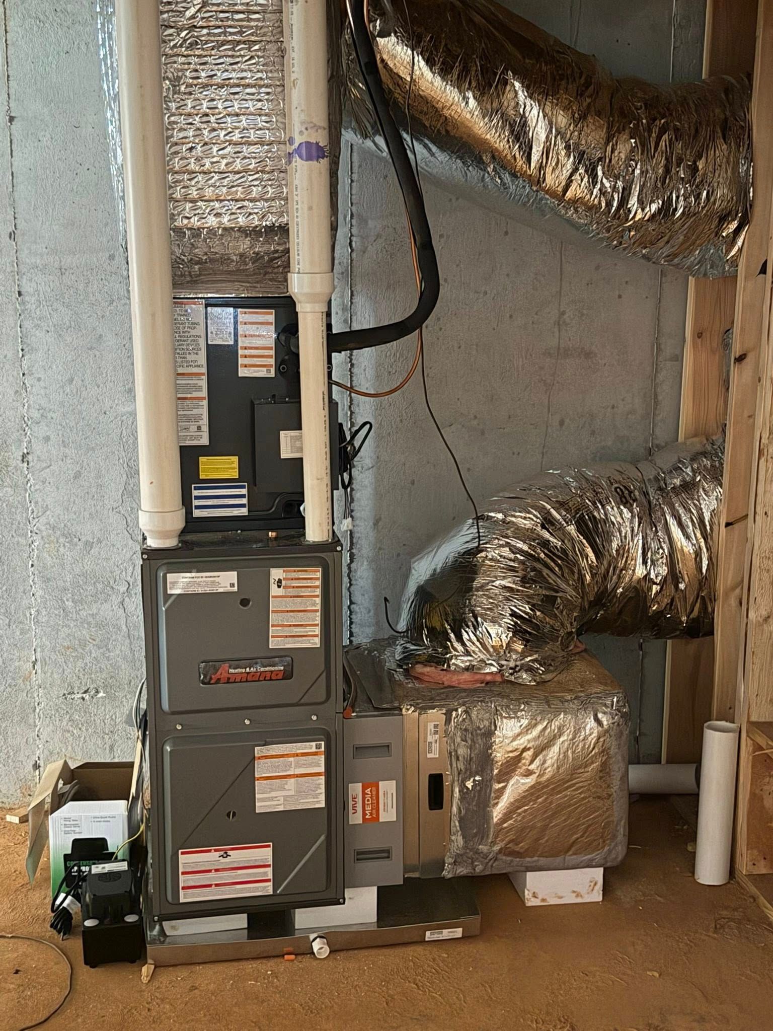 Two stacked HVAC furnaces in a basement utility room with silver ductwork and exposed pipes.