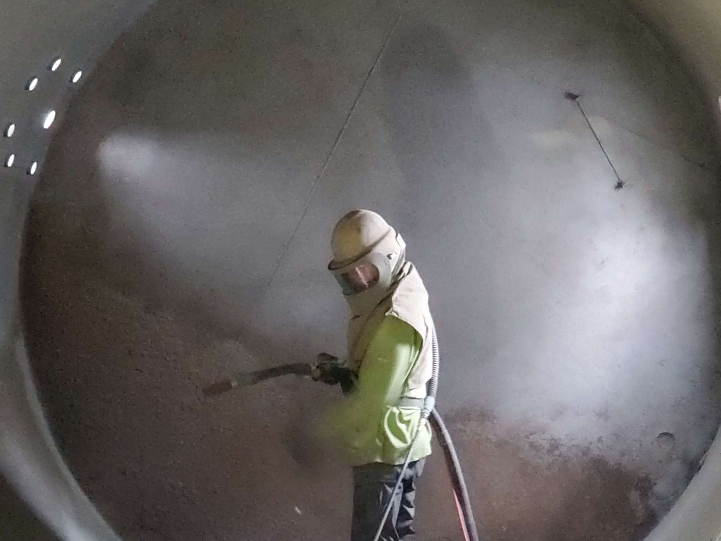 A man wearing a mask is spraying something in a large tank.