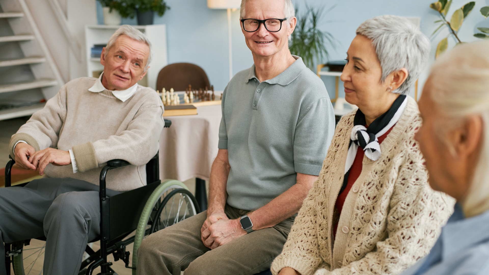 Residents chatting in a bright care home lounge, with one seated in a wheelchair and smiling